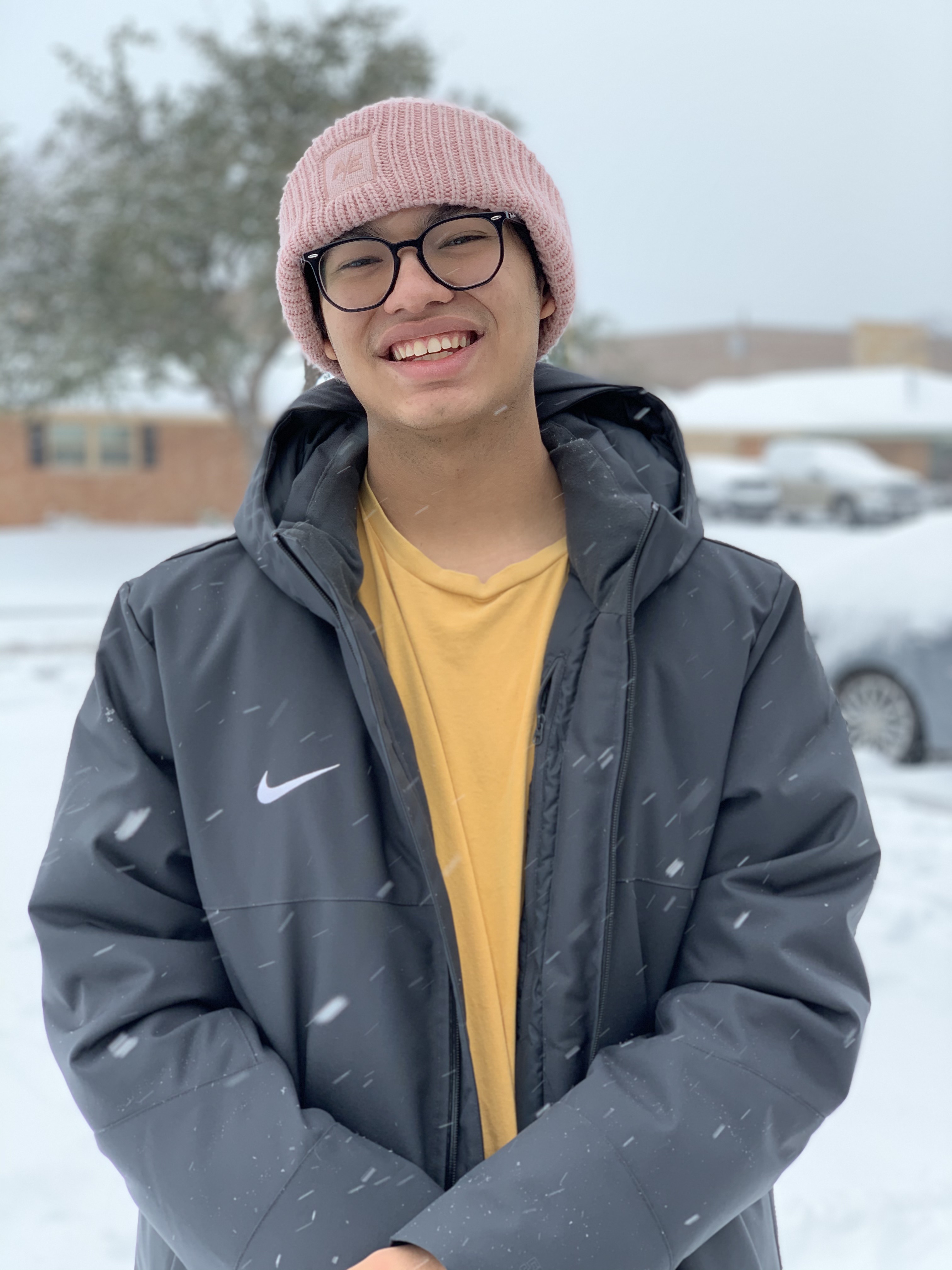 Photo of Nathan wearing a pink bennie, grey jacket, and yellow shirt. It is snowing.